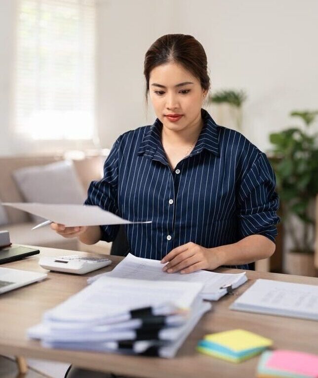 A professional female virtual legal assistant in a navy blue pinstriped shirt reviewing case files and legal documents at a desk.