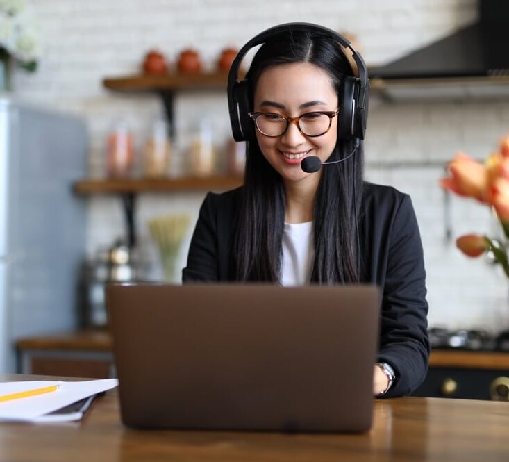 Asian woman smiling while communicating through a headset and providing support