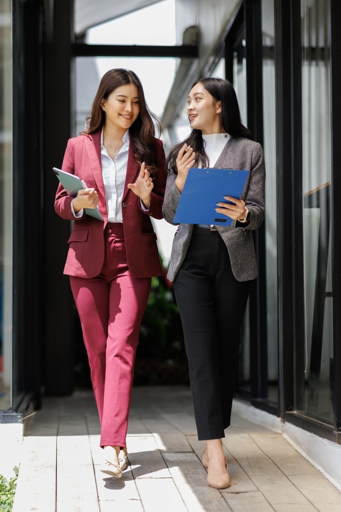 Two young Asian virtual legal assistants walking outside a business office center, dressed professionally.