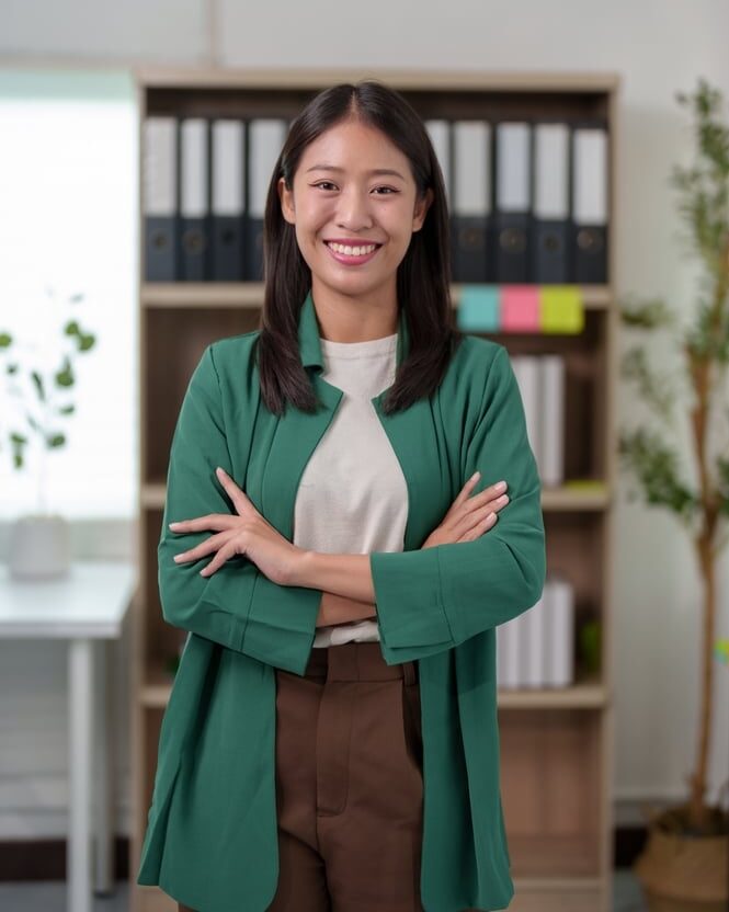 A smiling female virtual legal assistant in a green blazer standing with arms crossed in front of a shelf of legal case files, representing organized administrative support.