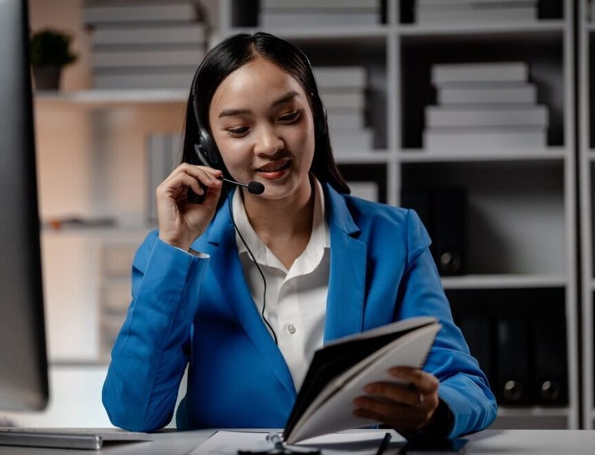Asian female virtual legal assistant wearing headphones, speaking with clients in a professional support setting.