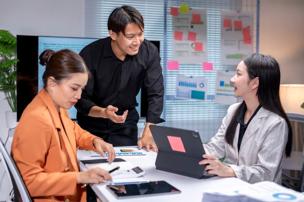 A team of virtual legal assistants in corporate attire collaborating on case strategy and data analysis in a modern office with a digital display and planning board.